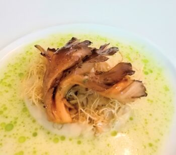 Plate of noodles topped with sliced braised meat and a light green oil splash around the edges.