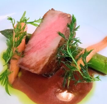 Cooked meat slice garnished with fresh dill on a pale plate, close-up view.
